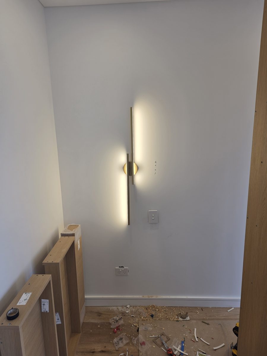 Fit-off: slim vertical brass wall light lit, with fit-off debris still on the floor, Picnic Point duplex