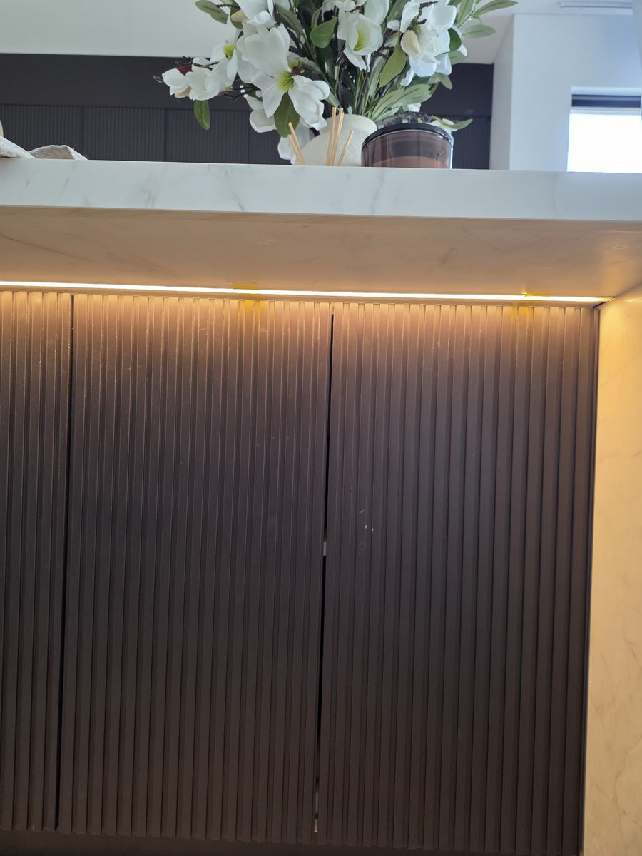 LED strip under a stone kitchen island over dark fluted doors, Picnic Point duplex